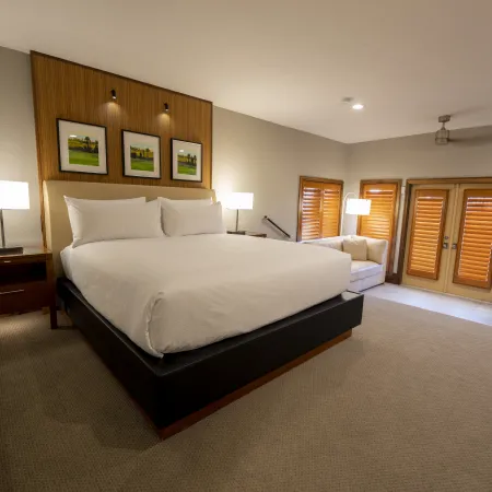 An image of an Evermore Orlando Resort Villa bedroom featuring a plush king-sized bed, a small step down towards a pull out couch and doors out to an exterior patio.