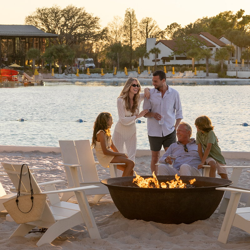 Image of a multi-generational family enjoying time together by a fire pit near Evermore Bay at Evermore Orlando Resort.