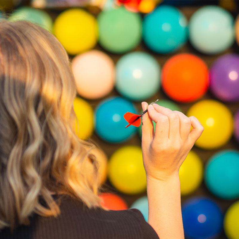 Image of a woman with a dart in her hand playing the Balloon Pop carnival game.