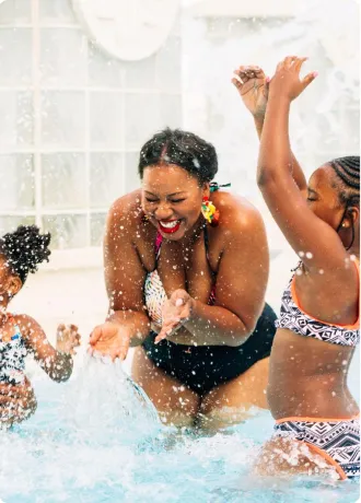Mother with two daughters standing in pool using hands to splash each other with water