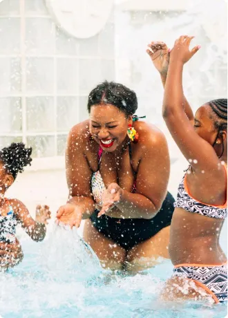 Family Splashing in Pool Mother with two daughters standing in pool using hands to splash each other with water