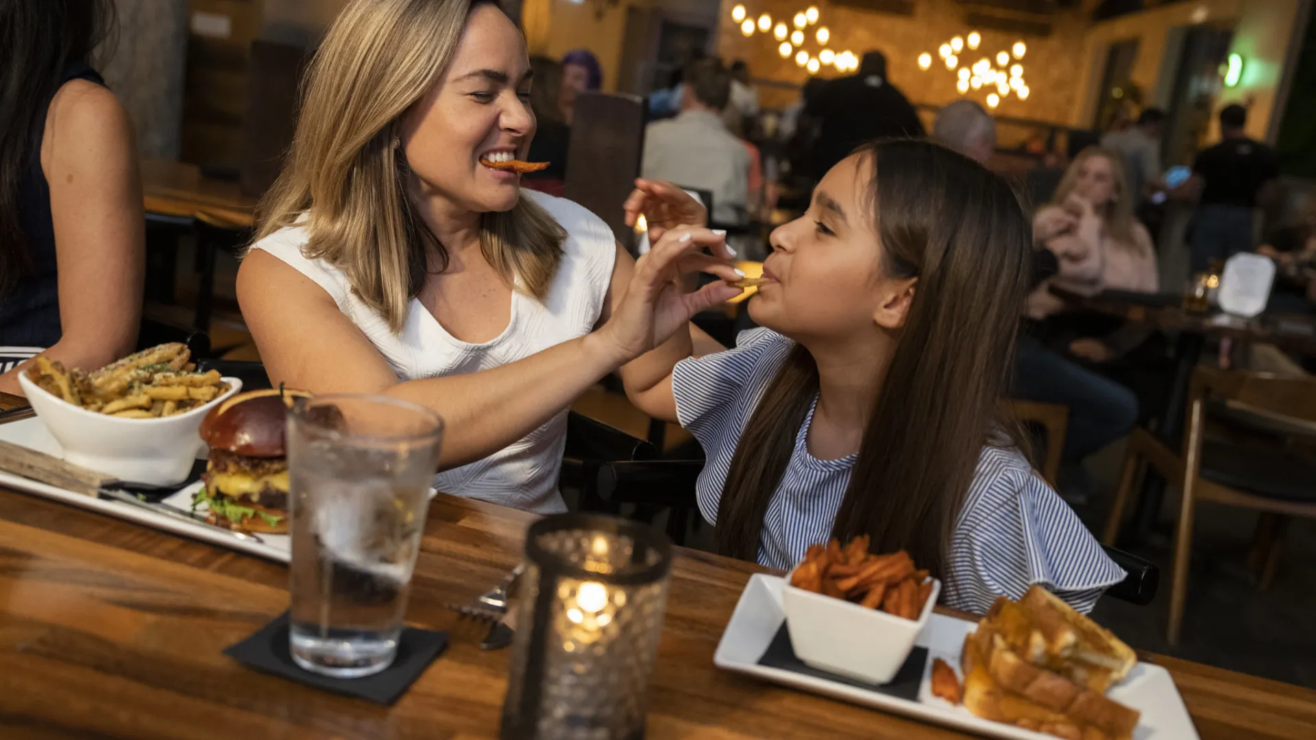 Mother and Daughter playfully feeding each other at dinner