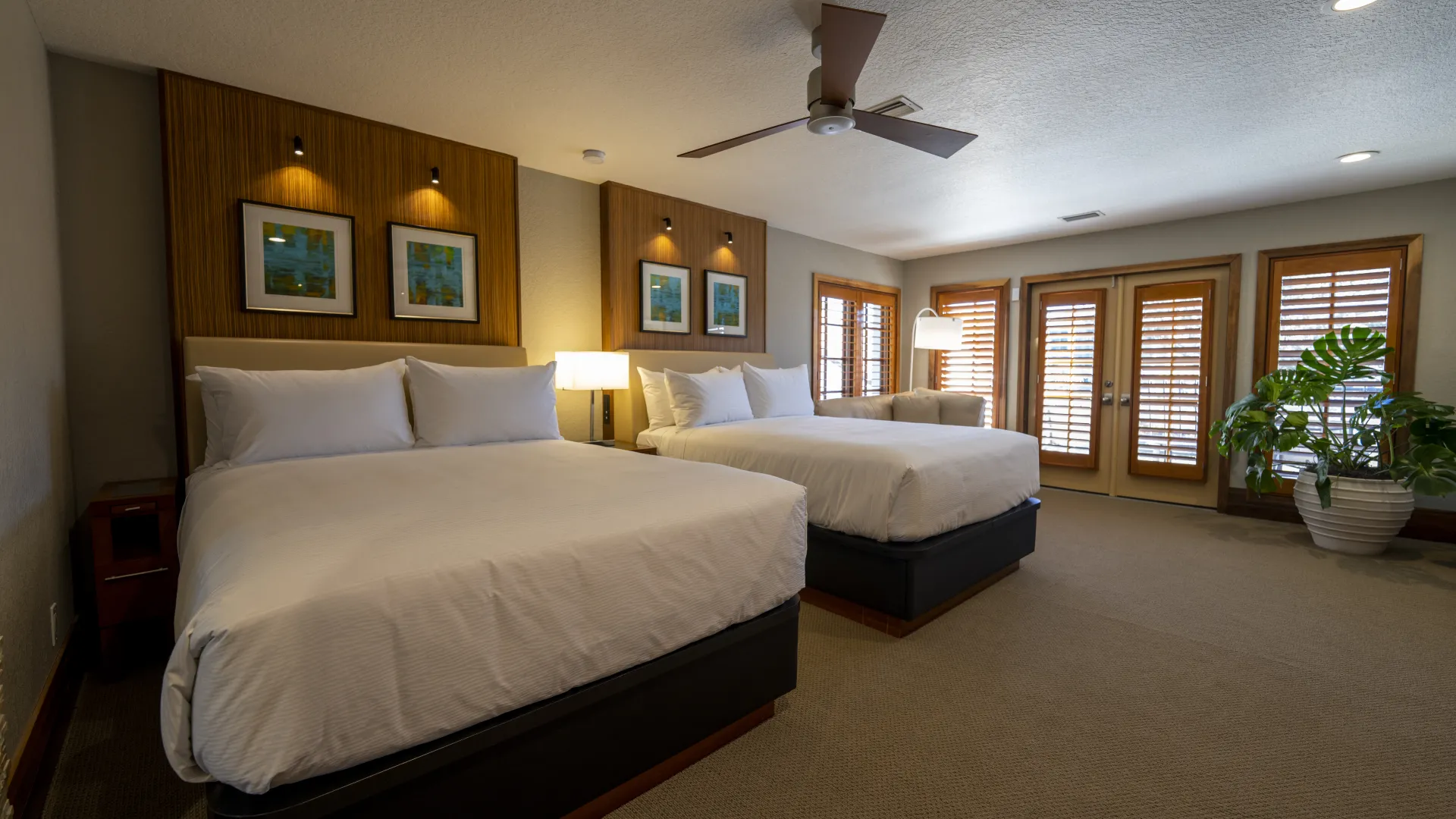 An image of an Evermore Orlando Resort Villa bedroom featuring 2 comfortable queen-sized beds inside of a large bedroom and a set of double doors leading out to an exterior patio. 
