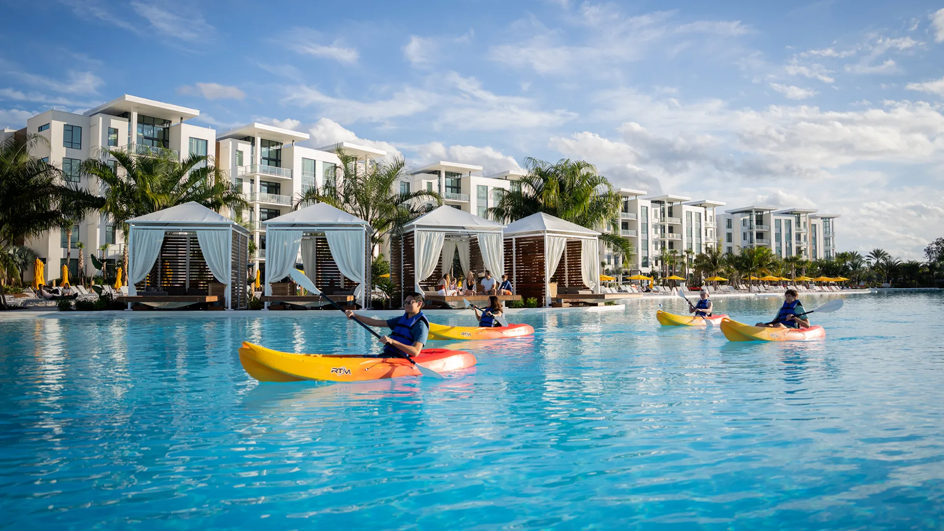 A wide shot of the Evermore Bay beach complex featuring guests enjoying complimentary kayaks as the paddle across the crystal blue waters of Evermore Bay