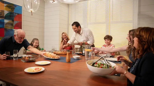 An image of a family sitting around the dinner table enjoying a Ready To Heat meal in a vacation rental house at Evermore Orlando Resort.