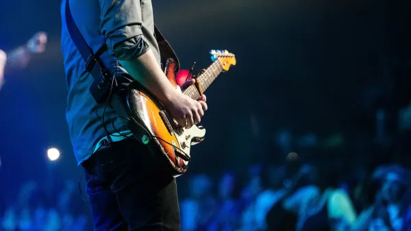 Image of a man playing an electric guitar at an outdoor concert.