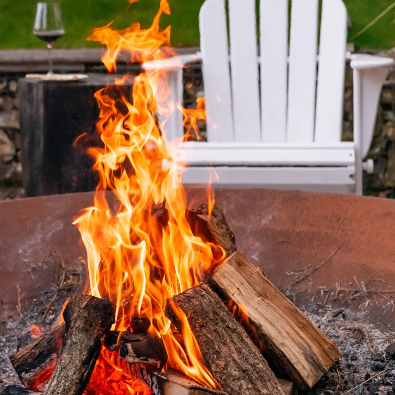 Fire Pit during Daytime Fire blazing in firepit with empty chair and wine glass in background