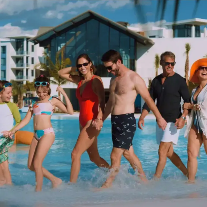 This is an image of a multi-generational family walking along the waters edge of Evermore Bay. The family is six people including, two children, two parents, and two grand parents. The entire family unit is smiling and are enjoying spending time together at Evermore Orlando Resort.