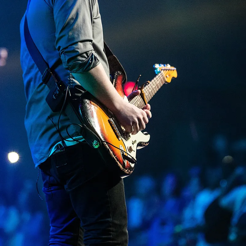 An image of a man playing an electric guitar at an outdoor concert.