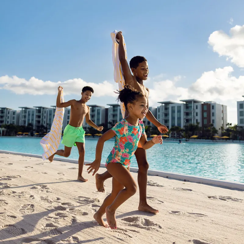 An image of three kids smiling while playing on the beach by Evermore Bay at Evermore Orlando Resort.