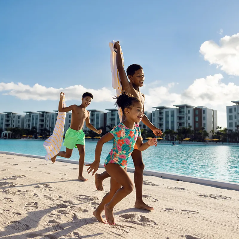 An image of three kids smiling while playing on the beach by Evermore Bay at Evermore Orlando Resort.
