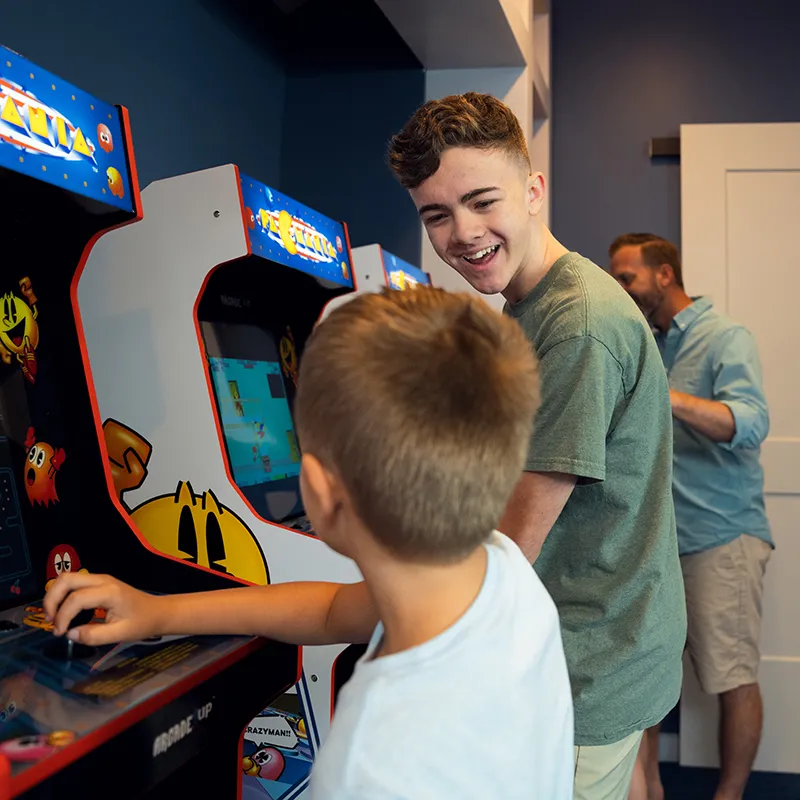 Arcade Games in an Evermore House Image of kids laughing while playing arcade games inside their vacation home at Evermore Orlando Resort.
