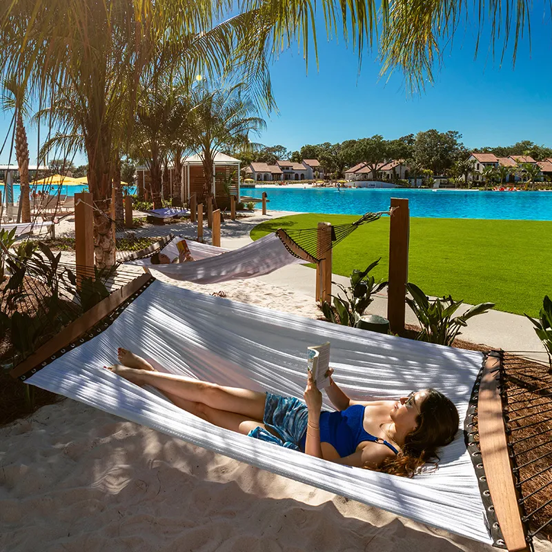 Guest Relaxing in Hammock Grove Image of a woman reading a book while relaxing in a hammock by Evermore Bay at Evermore Orlando Resort.