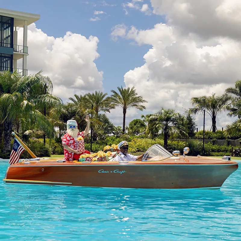 Image of Santa Claus riding on the Chris-Craft boat across Evermore Bay on his way to greet guests at Evermore Orlando Resort.