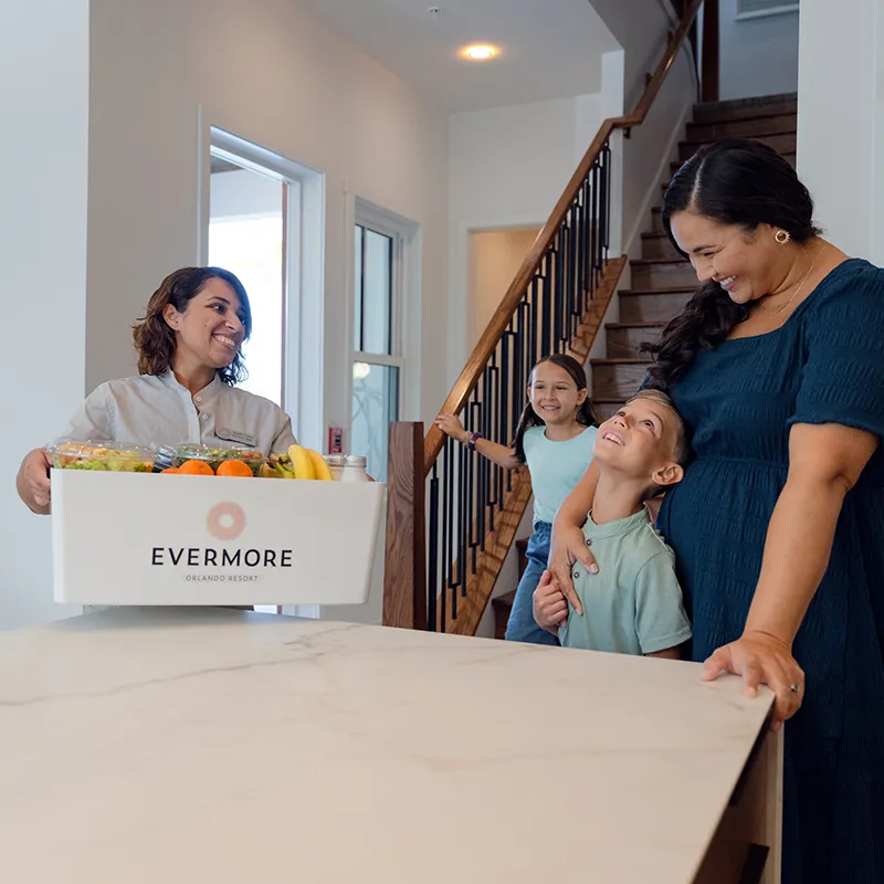 Image of a Culinary Concierge team member delivering groceries to a family in their vacation home at Evermore Orlando Resort.
