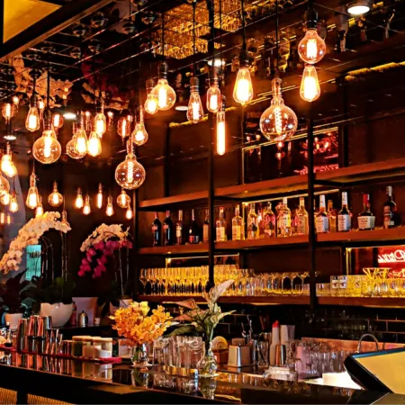 Shot of empty bar with hanging Edison light bulbs and stocked shelves of bottles and glassware