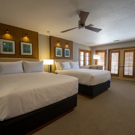 An image of an Evermore Orlando Resort Villa bedroom featuring 2 comfortable queen-sized beds inside of a large bedroom and a set of double doors leading out to an exterior patio. 