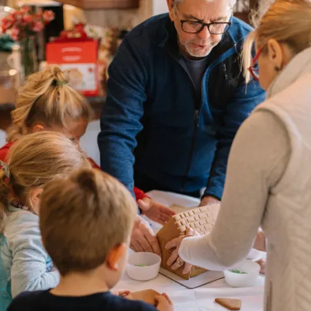 Image of a family decorating a gingerbread house together.