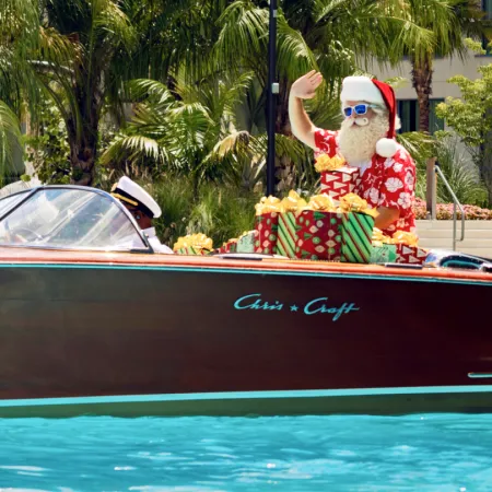 Image of Santa Claus riding on the Chris-Craft boat across Evermore Bay on his way to greet guests at Evermore Orlando Resort.