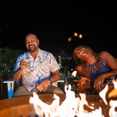 Image of adults laughing while enjoying drinks by a large firepit at Evermore Orlando Resort.